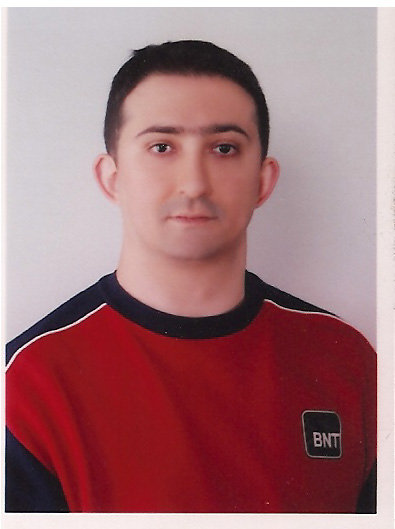 head shot of a dark haired young man with fair complexion looking straight at camera from white wall wearing a collarless shirt which looks a bit like a star trek costume